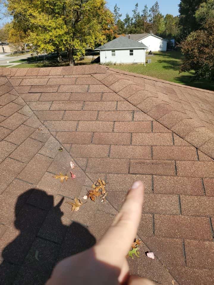 A person is pointing at a damaged shingle roof.