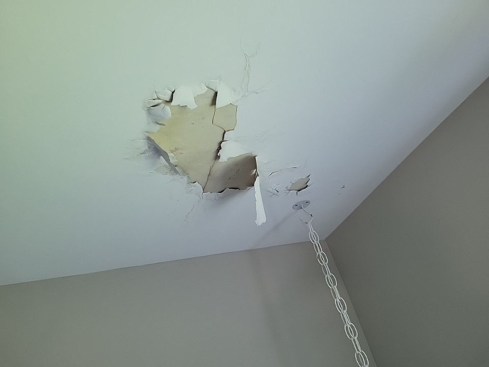 A hole in the damaged ceiling of a room after a hail storm.