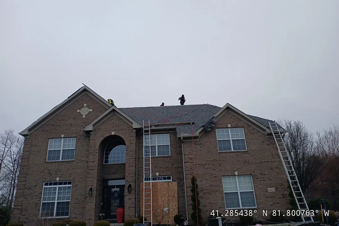Two workers on the roof of a brick house, possibly conducting repairs or inspection as part of our work.