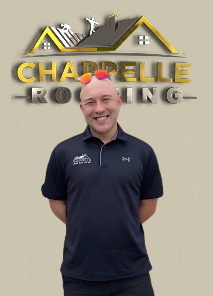 Smiling man in a polo shirt standing in front of an "About Us" sign with the text "Chappelle Roofing" and a logo featuring a house roof and three figures.