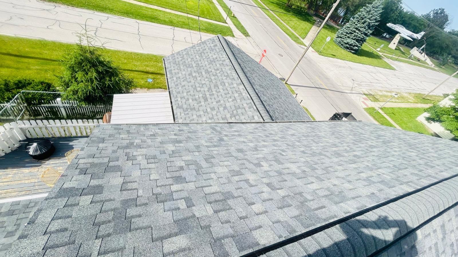 A rooftop view showing gray asphalt shingles on building roofs with a street, grass lawns, and a model airplane monument in the background highlights our work in maintaining top-notch quality.