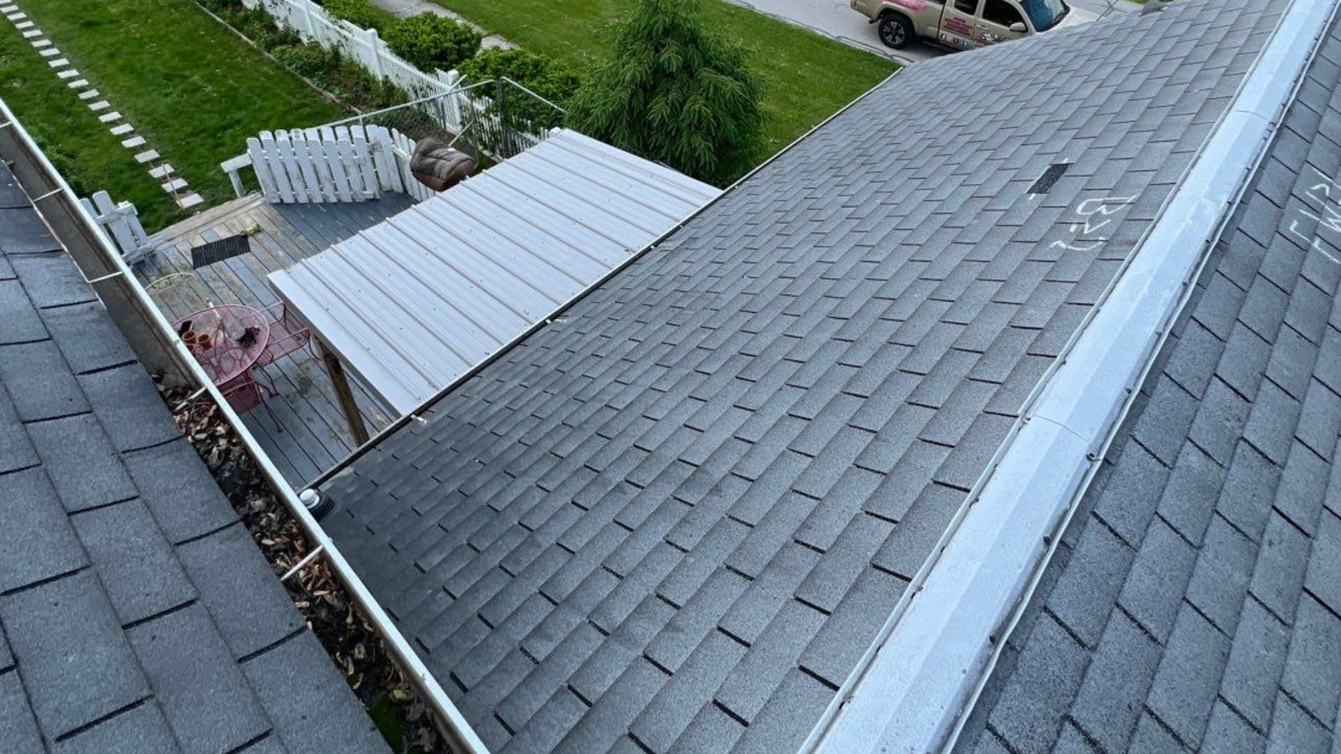 Our work is showcased in the view from a rooftop with gray shingles, a well-maintained gutter, and a fenced yard featuring a covered patio below.