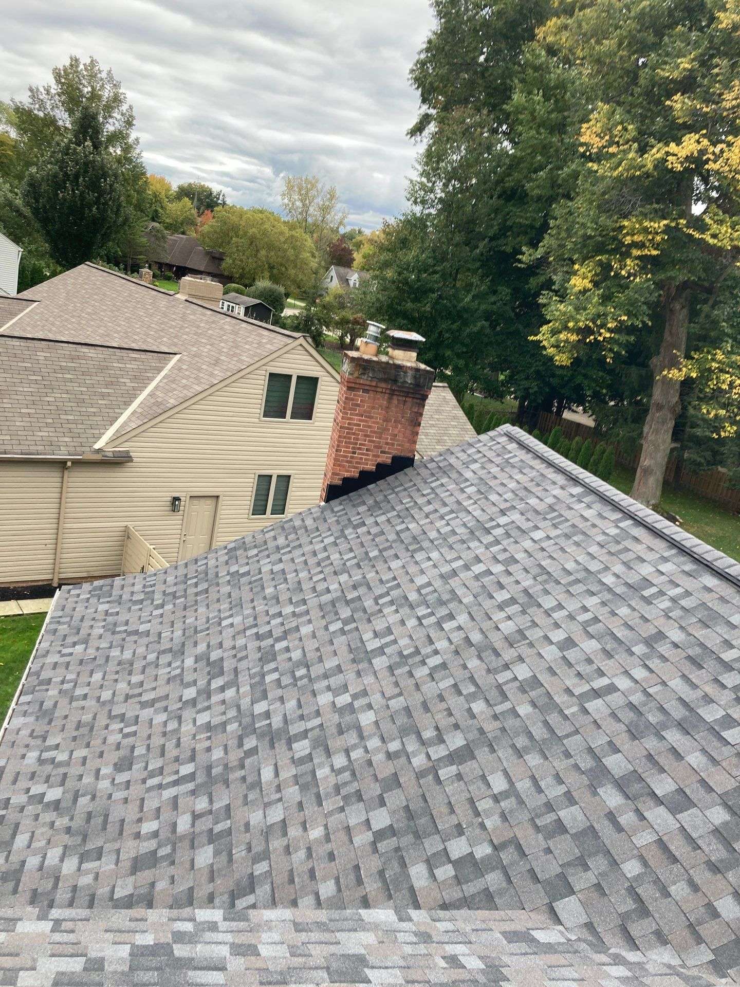 From the rooftop adorned with gray shingles and a sturdy brick chimney, you can admire our work—a charming residential neighborhood nestled among lush trees and well-kept houses.